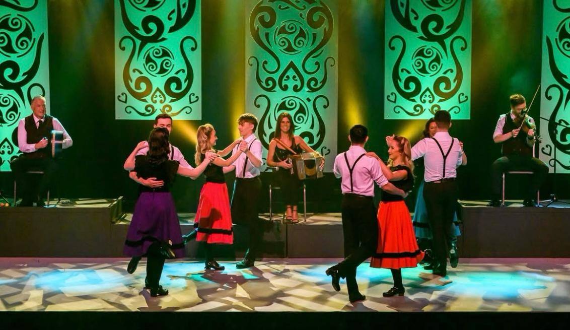 Dancers and live musicians on stage at Celtic Steps in Killarney, Celtic patterns lit green behind them